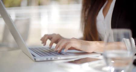 Businesswoman typing on a laptop computer as she sits at a table with a jug of fresh water  closeup...