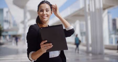 Smiling attractive young professional woman standing in a high key urban environment surfing the internet on a tablet computerの写真素材