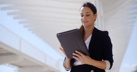 Elegant businesswoman standing on a seafront promenade holding a tablet computer in her hands looking at the cameraの写真素材