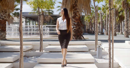 Elegant young businesswoman walking through a park looking off to her right as something catches her interest  full length approaching the cameraの写真素材
