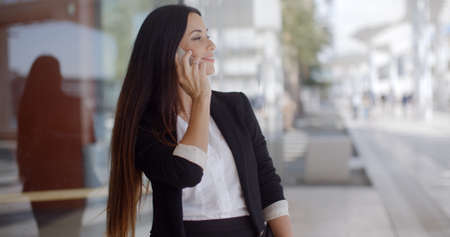 Thoughtful gorgeous woman chatting on a mobile phone in an urban environment looking off to the side with a pensive expressionの写真素材