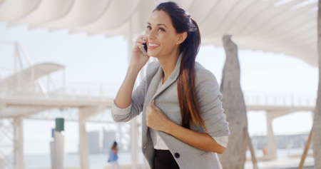 Attractive stylish young woman talking on her mobile phone in a high key white urban environment ...