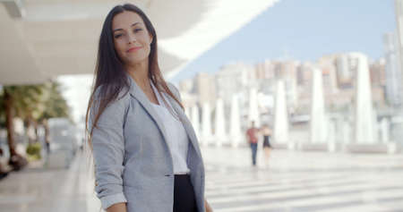 Confident young woman with a friendly smile standing outdoors on a waterfront urban promenade looking at the camera  upper body with lateral copyspaceの写真素材