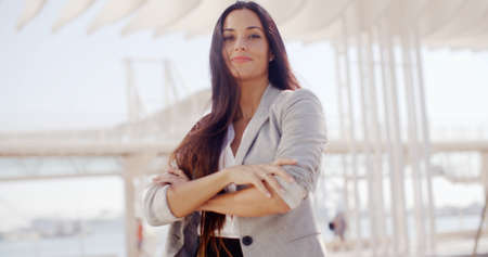 Confident attractive woman with long brown hair standing in the center of the frame with folded arms smiling at the camera  high key bilateral copyspaceの写真素材