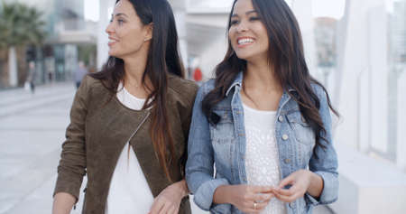 Two young women strolling down a high key white urban promenade towards the camera smiling and chatting  upper body viewの写真素材
