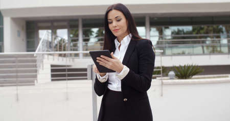 Stylish businesswoman using her tablet computer as she stands in an urban square or forecourt reading information with a serious expression  with copy spaceの写真素材