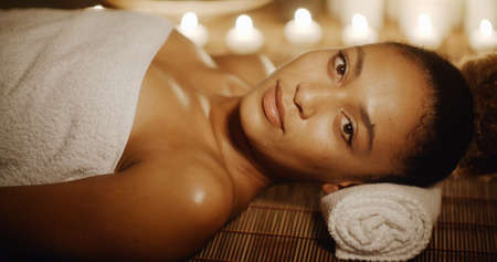 Young woman relaxing at beauty spa by candle light and looking at camera