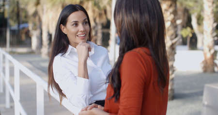 Gorgeous stylish young woman standing outdoors on an urban promenade chatting to a friendの写真素材