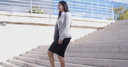 Serious young business woman in high heel shoes walking up long flight of marble stairs outdoors