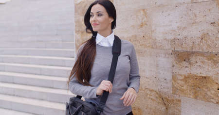 Grinning young woman in sweater holding bag and looking over with confident expression next to large marble wallの写真素材