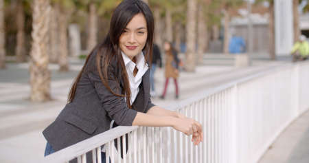 Relaxed thoughtful young woman leaning on white metal railings outdoors in an urban park looking to...