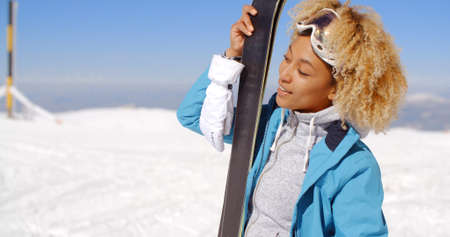 Single beautiful woman in blond curly hair and goggles holding skis with copy space over snowy backgroundの写真素材