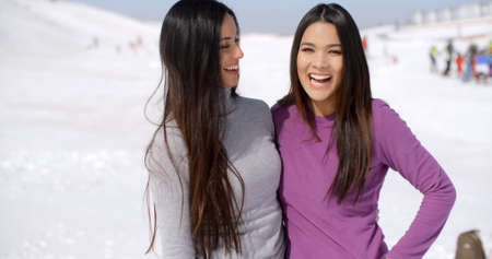 Laughing vivacious young women at a winter ski resort standing in the snow smiling happily at the camera  close up upper bodyの写真素材