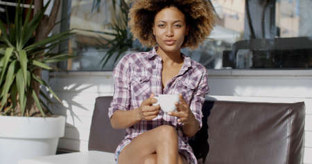 Portrait of a young woman sitting outdoors in beach cafe and drinking tea or coffeeの写真素材