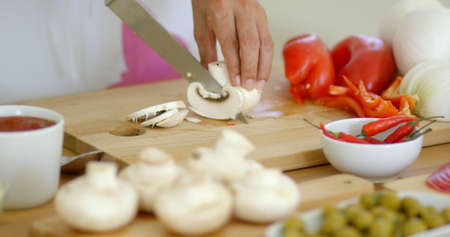 Housewife preparing dinner slicing fresh mushrooms on a wooden chopping board on a kitchen counter  close up low angle on her handsの写真素材