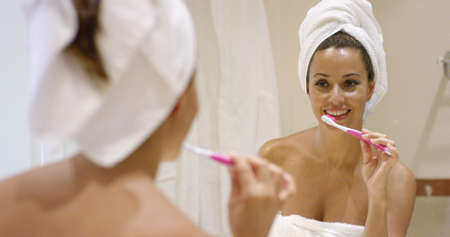 Young woman cleaning her teeth with a toothbrush in the bathroom standing in front of the mirror...