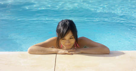Brown haired woman thinks to herself and smiles while wearing a swim suit and standing in a pool