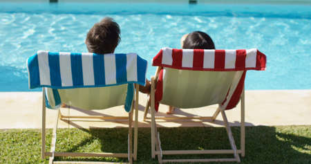 Couple relaxing in colorful deck chairs at the pool enjoying the hot summer sun  view from the rear with just their head visibleの写真素材
