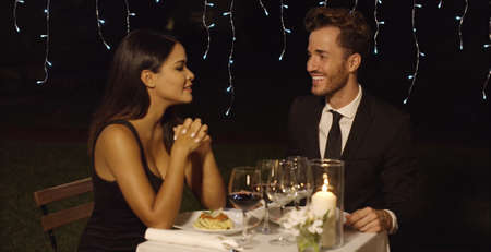 Handsome couple laughing while at restaurant during night time date over plates of spaghettiの写真素材