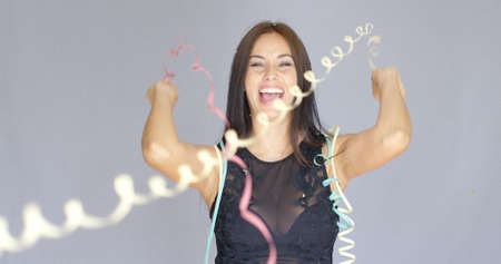 Vivacious laughing young woman in a black cocktail dress enjoying a party to celebrate the New Year  over a grey backgroundの写真素材