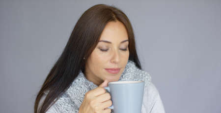 Beautiful long haired, brunette woman holding in her hand cup of hot drink. She wearing woolen scarf...