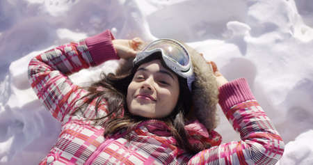 Young woman lying on snow with ski gogglesの写真素材