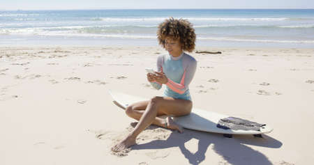 Female sitting on beach using smartphoneの写真素材