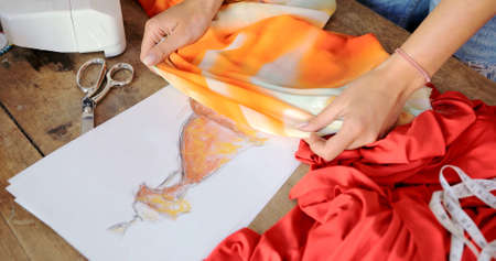 Crop female using sketch with drawn dress and choosing vibrant fabric in atelier.の写真素材