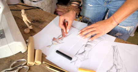 Crop faceless shot of female tailor standing near table in and drawing sketches of dress.の写真素材