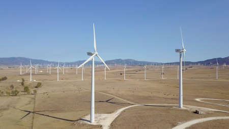 Aerial shot of white windmills placed in rows on terrains of tropical desert under blue sky and...
