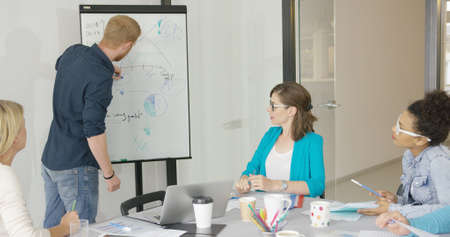 Man drawing simple graphic on board and presenting new information on project for coworkers at table...