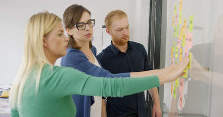 Side view of three young workers putting stickers on glass wall of contemporary office creating new...