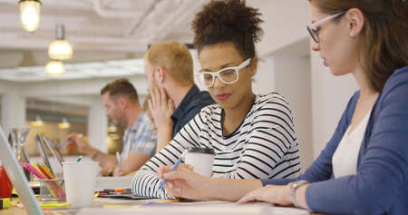 Young women working with documents while posing at table on background of male coworkers.の写真素材