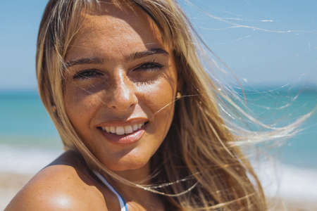 Headshot of content pretty blond woman with flying hair in wind looking at camera on background of ocean.の写真素材
