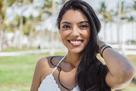 Portrait of beautiful ethnic brunette with long hair smiling at camera on background of tropical park.の写真素材
