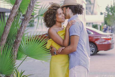 Side view of adult ethnic man and woman standing together and embracing on the street in sunny day.