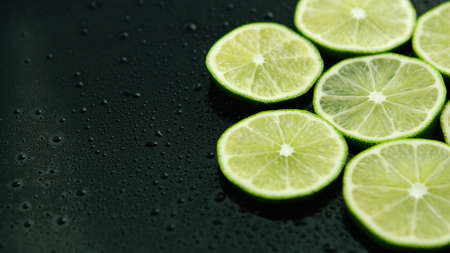 From above slices of fresh green sour lime on dark table with water dropsの写真素材