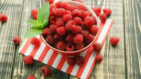 From above shot of bowl full with red raspberries and served on napkin on wooden table