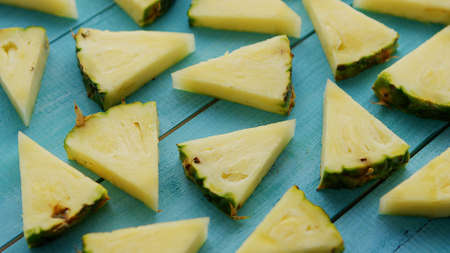 From above appetizing ripe unpeeled pineapple triangle pieces placed on blue wooden background