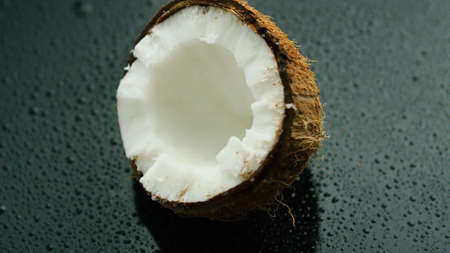 Closeup shot of delicious white coconut half in rough brown shell lying on wet glass surface