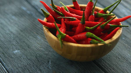 Closeup shot of small wooden bowl filled with pile of fresh and ripe red spicy chili peppers on wood...