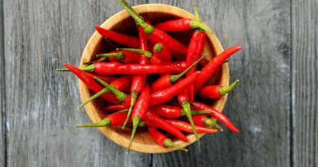 From above shot of round wooden bowl filled with pile of bright red chili pepper and composed on...
