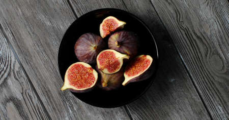 From above view of black round plate with delicious ripe figs cut into halves and served on gray wooden tableの写真素材