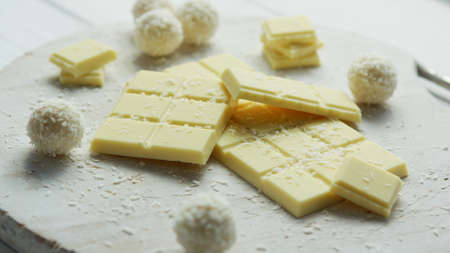 Closeup of arranged white chocolate bars with coconut sweets on wooden board