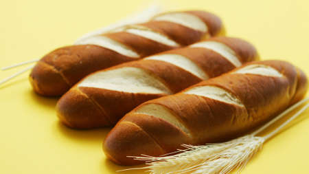 Closeup of golden baguettes with few soft wheat ears lying in row on yellow background