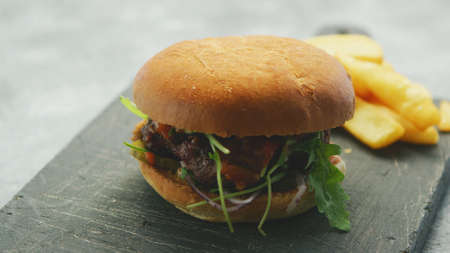 Closeup of burger with salad and meat served with golden fries on black rough board in daylightの写真素材