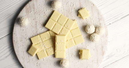 From above shot of wooden round board with bars of white chocolate and coconut sweets