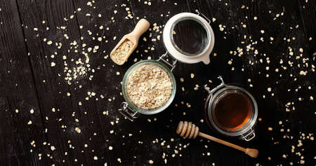 From above view of oat and honey in glass jars placed on black wooden backgroundの写真素材
