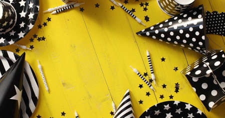 From above view of decorative paper hats and plates in black and white colors laid in circle on yellow wooden backgroundの写真素材