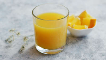 Closeup shot of glass filled with freshly squeezed orange juice and composed on table with small bowl of cut orangeの写真素材